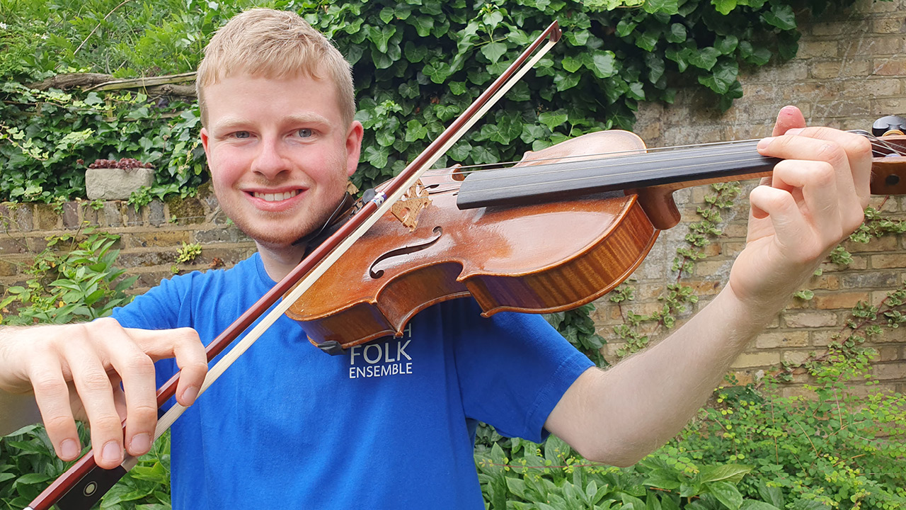 Musician playing viola and smiling into the camera, with plants and garden wall in the background