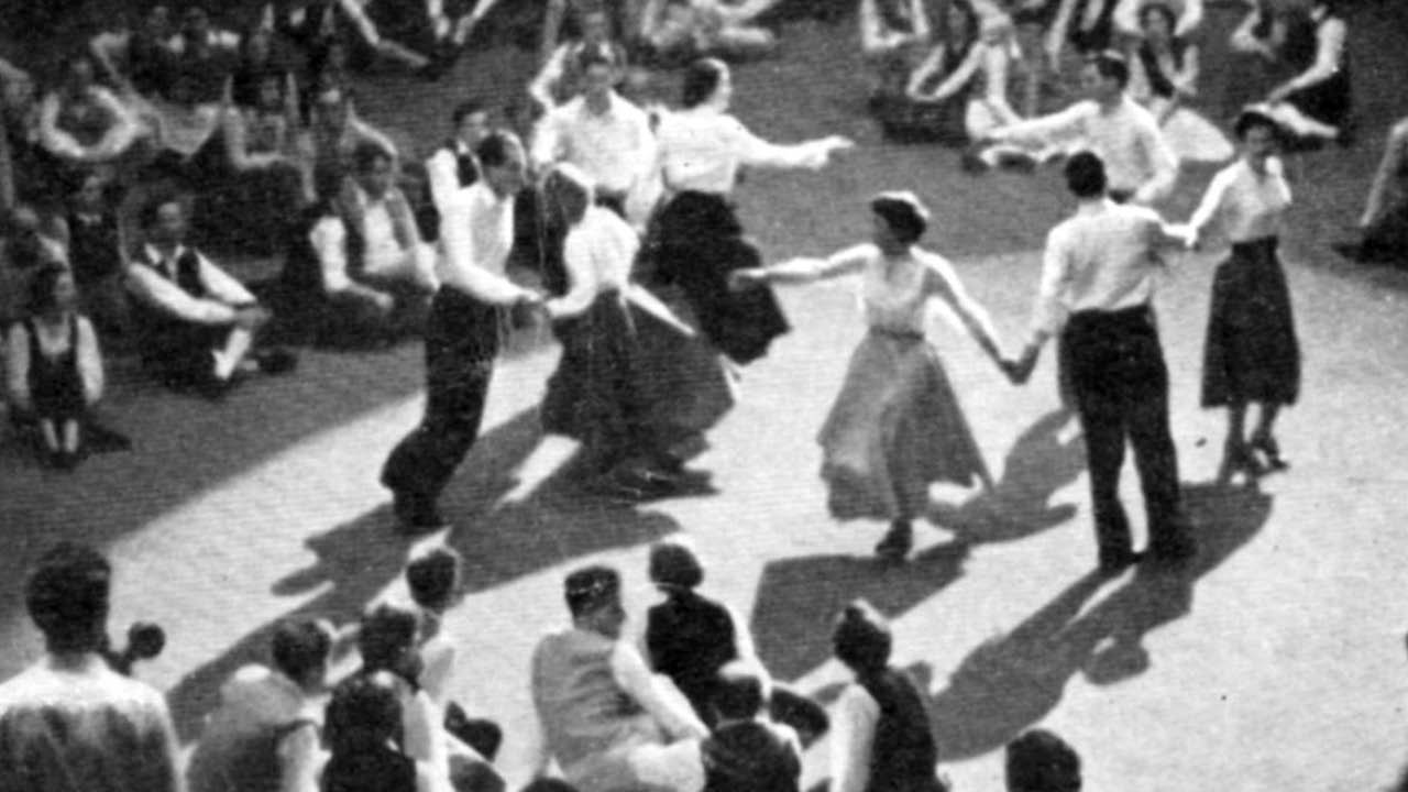 historical photo taken from above of dancers in a ring with groups sitting on the ground around them 