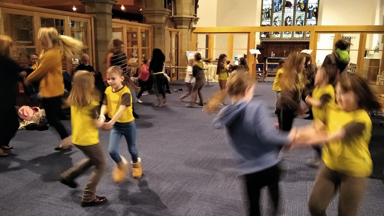 Children and a few adults dancing enthusiastically in a community hall