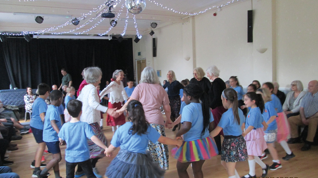 Two circles of dancers: seniors in centre, surrounded by a larger number of children 