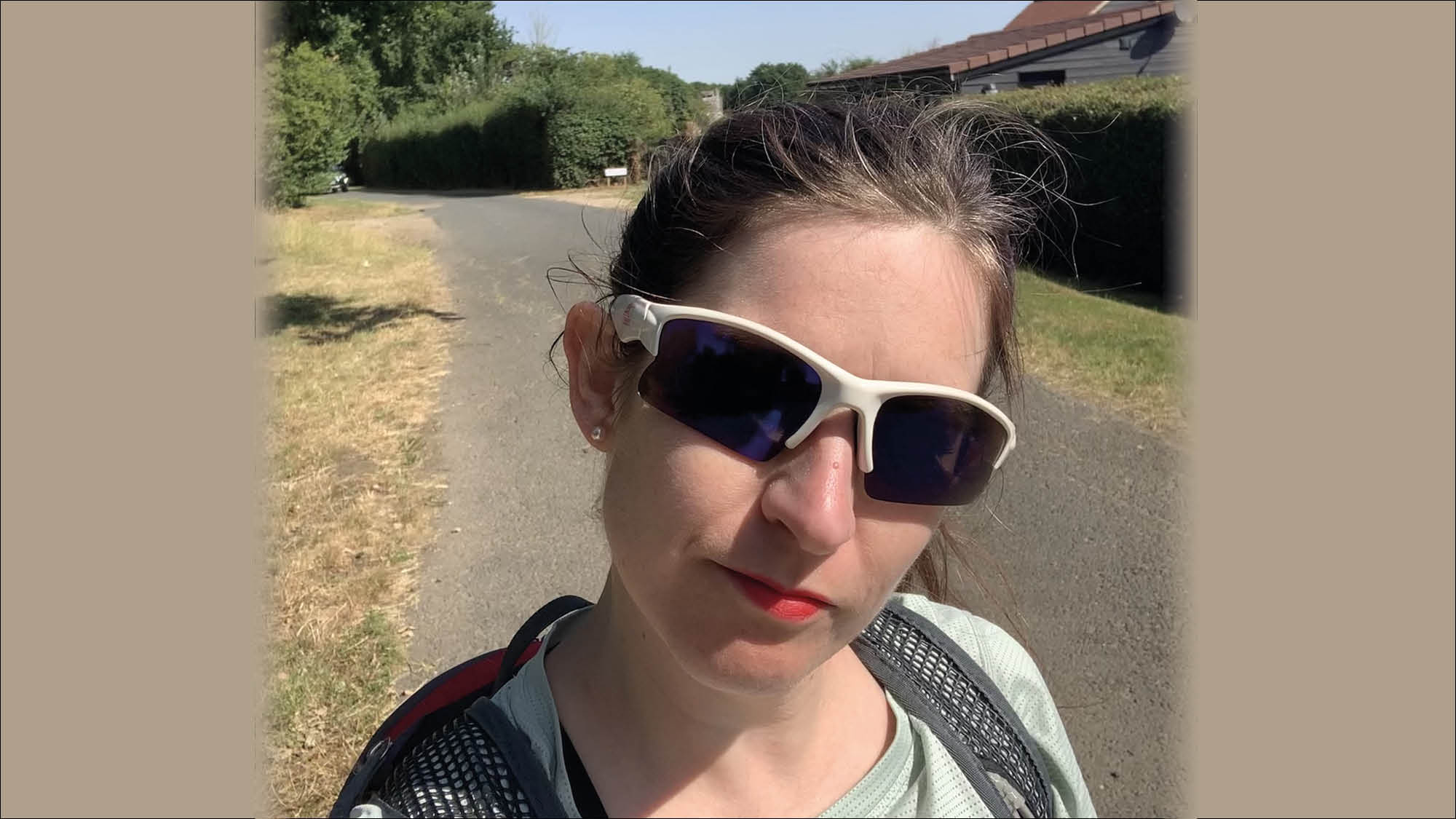 Selfie of Tiffany wearing sunglasses in bright sunshine, with small empty road behind 