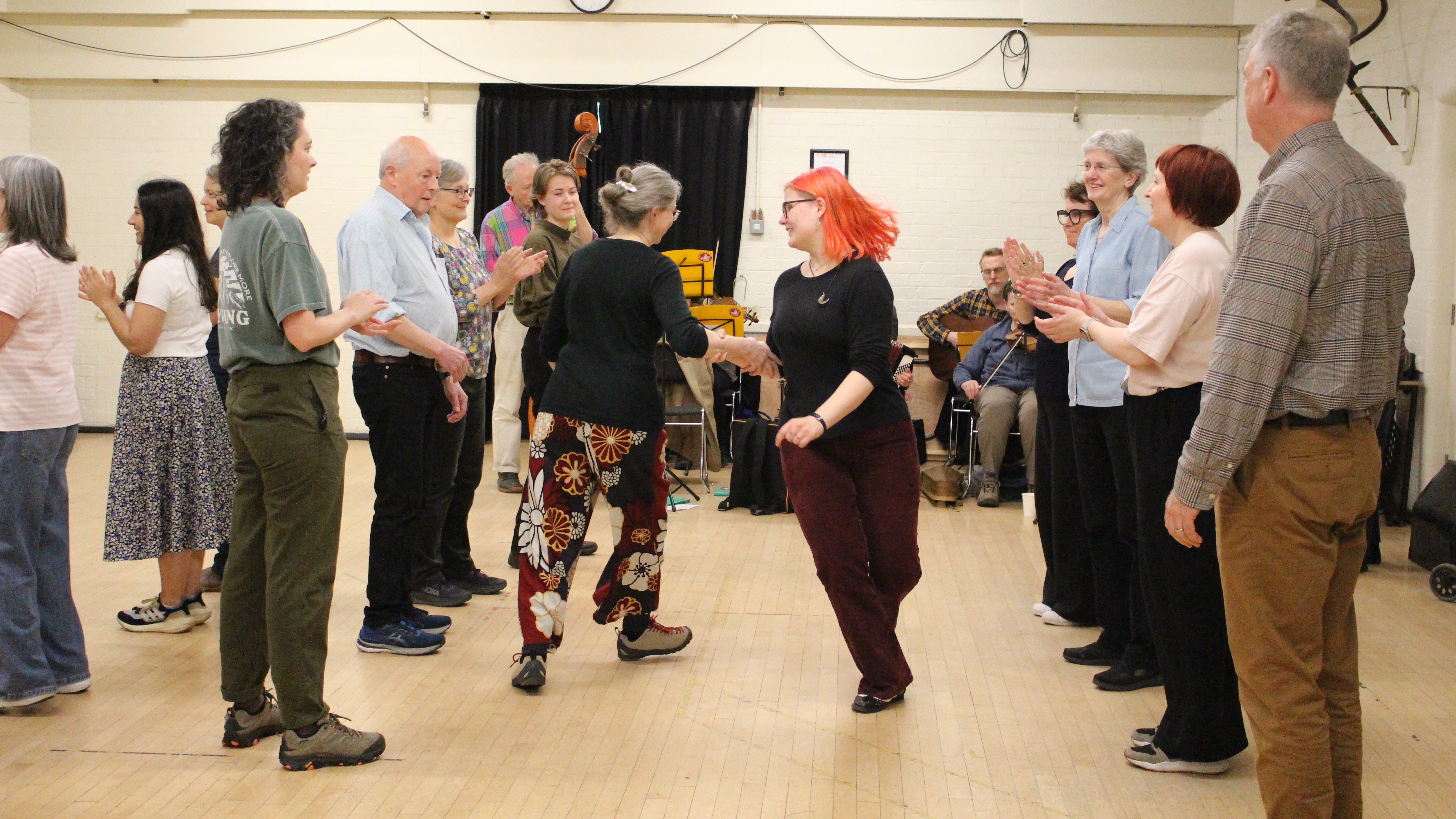 women and male dancers in a range of ages circling in a star shape, left hands in the centre