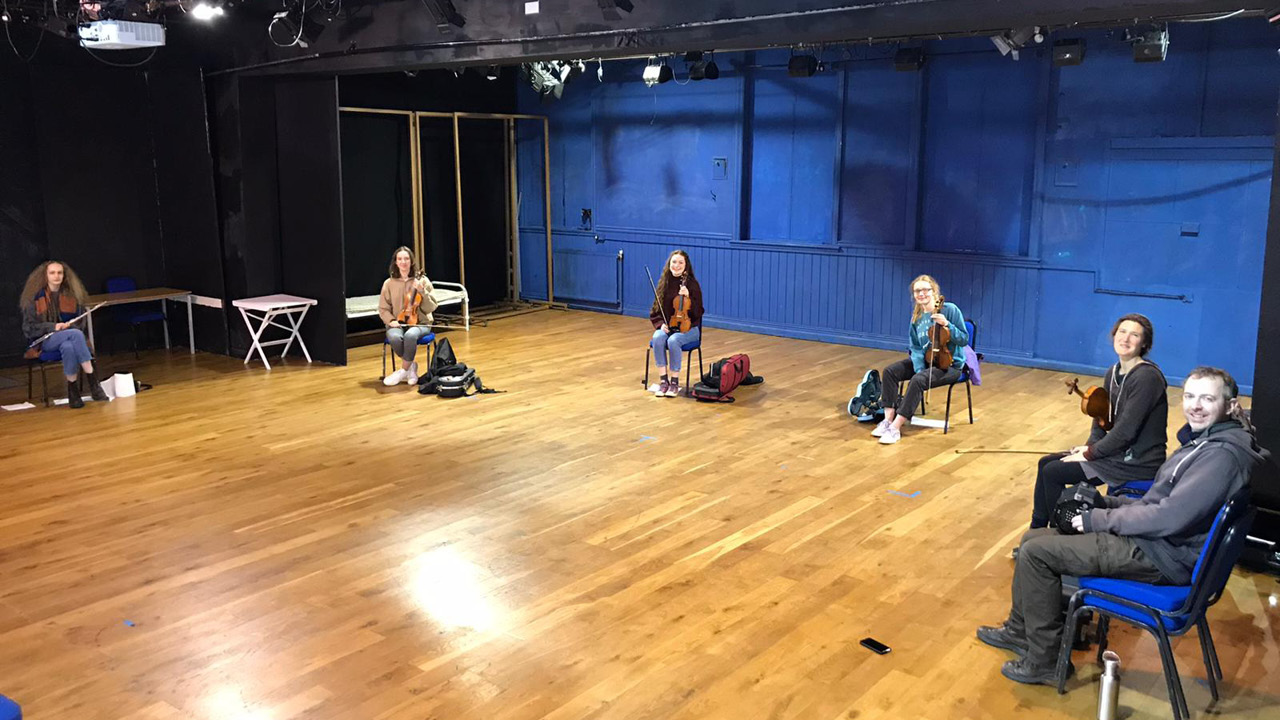 Young musicians with instruments, sitting in clear theatre space in Exeter