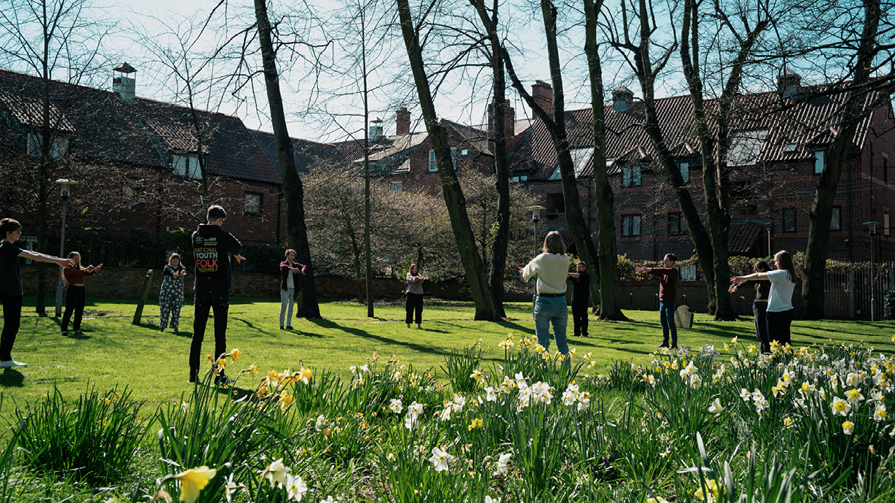 Young people standing in a circle and stretching in garden with spring flowers