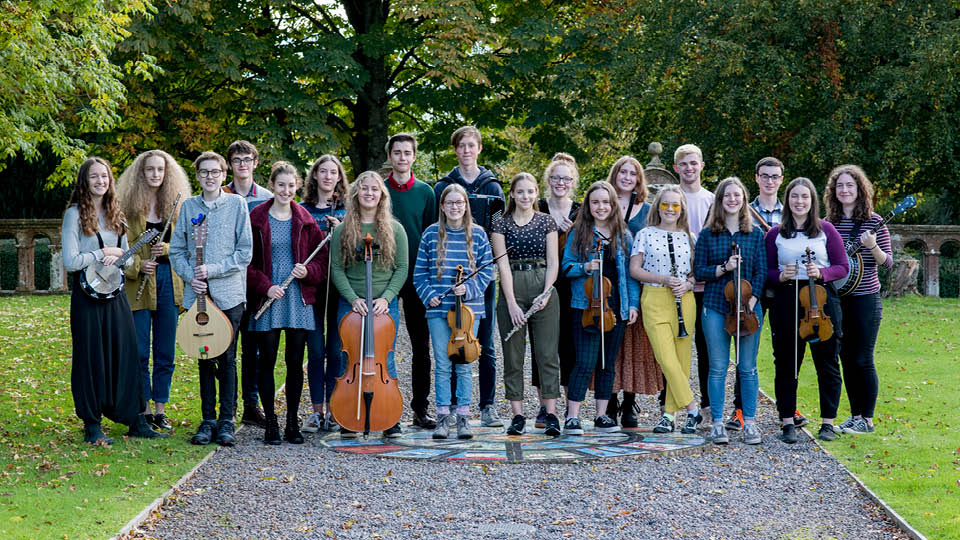 Ensemble of nearly 20 young people holding instruments and looking at camera