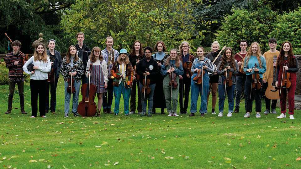 Ensemble of nearly 20 young people holding instruments and looking at camera