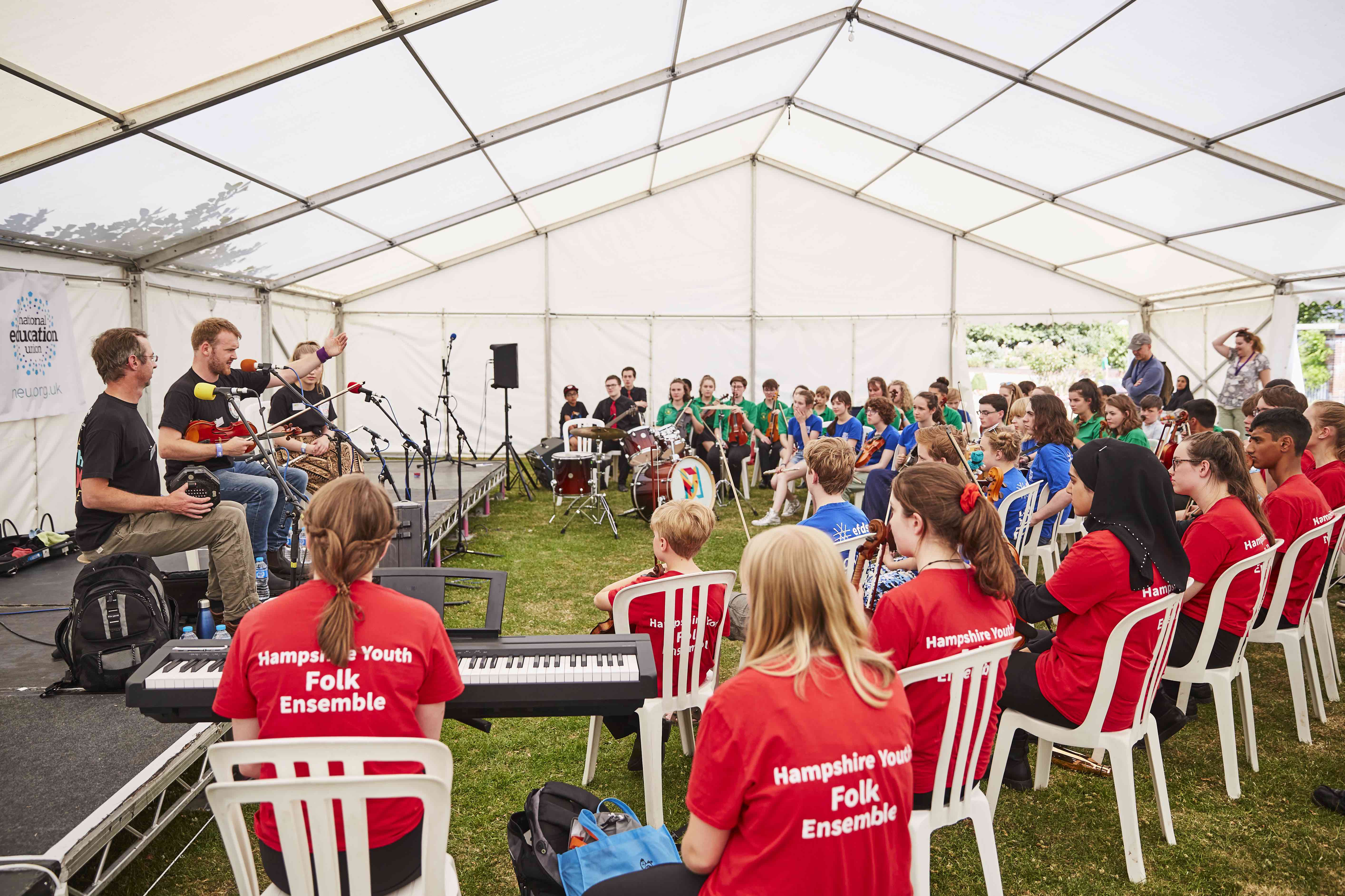 professional and young musicians playing together in a circle, in an outdoor marquee 