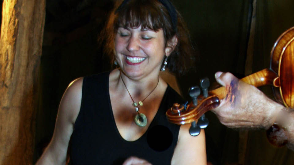 Smiling dancer, eyes down in focused enjoyment, with fiddle player in the foreground