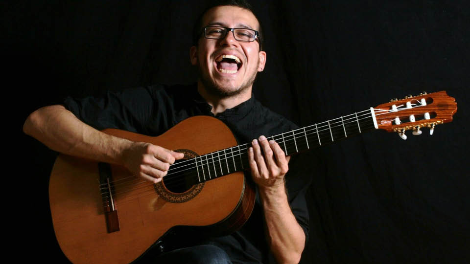 Man playing guitar and smiling very broadly, looking at camera
