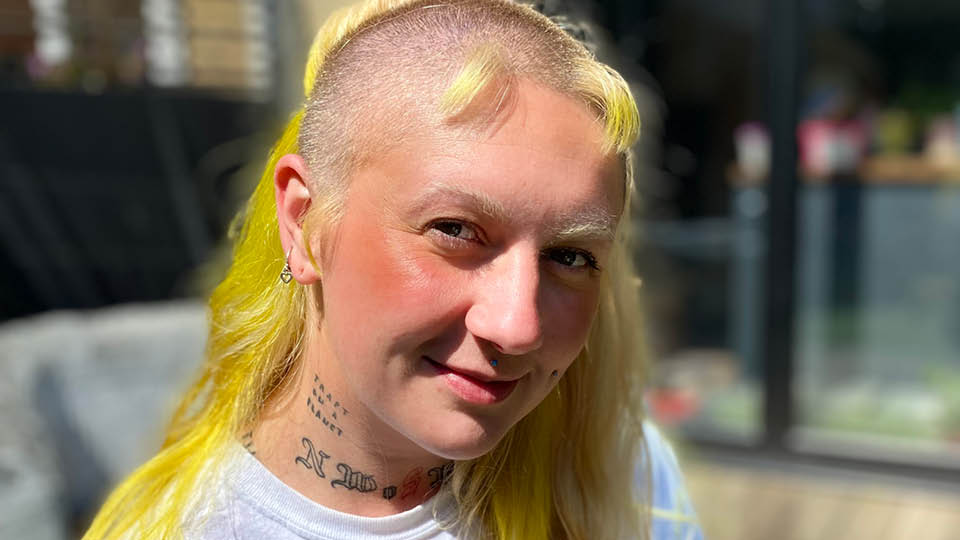 Woman with mostly shaven head and some long yellow hair